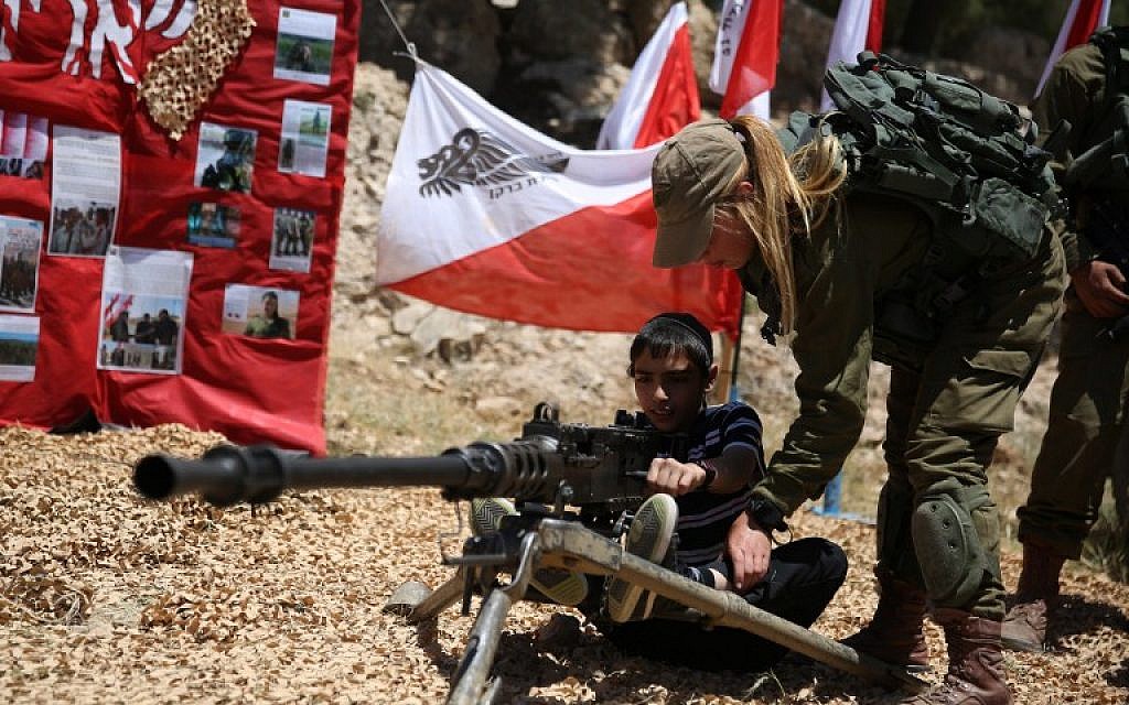 An IDF soldier shows a boy how to operate a machine gun near the West Bank settlement of Maale Adumim on May 12, 2016 during a traditional military weapon display as Israel marks its 68th Independence Day. (AFP PHOTO/GALI TIBBON)
