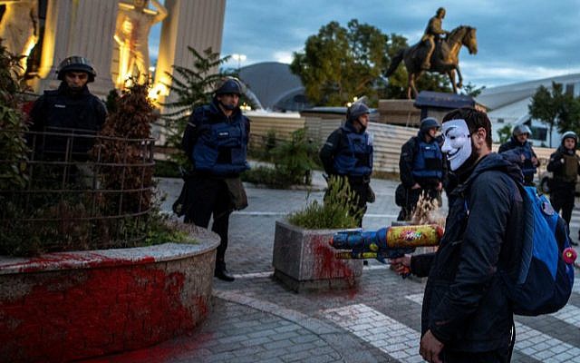 A protester wearing a mask uses a water gun to spray colored paint onto the facade of the Foreign Ministry building in front of the police cordon, during an anti-government protest in Skopje, Macedonia, on May 16, 2016, one of a series of anti-government protests over the past two years dubbed the Colorful Revolution. (Robert Atanasovski/AFP)