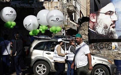 'Beirut Madinati' campaign workers hold balloons next to a poster showing Hezbollah leader Hassan Nasrallah, outside a polling station during the municipal elections in Beirut on May 8, 2016. (AP Photo/Hassan Ammar)