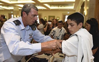 IDF Chief Rabbi Rafi Peretz teaches an IDF orphan how to put on tefilin for the first time at a Bar Mitzvah ceremony organized by the IDF Widows and Orphans Organization, in an undated photograph. (courtesy)