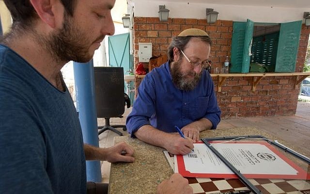 Rabi Aaron Leibowitz (C), the founder of Hashgach Pratit - Hebrew for private supervision -, which checks if restaurants abide by kosher practices, signs a certificate for the new bar Eitan Steinberg in the center of Jerusalem on June 8, 2016.(AFP PHOTO / MENAHEM KAHANA) Rabi Aaron Leibowitz (C), the founder of Hashgach Pratit - Hebrew for private supervision -, which checks if restaurants abide by kosher practices, signs a certificate for the new bar Eitan Steinberg in the center of Jerusalem on June 8, 2016.(AFP PHOTO / MENAHEM KAHANA)
