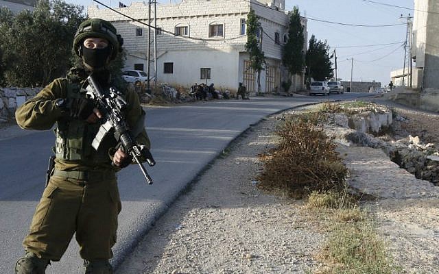 An IDF soldier keeps watch as Palestinians sit nearby after the army entered the village of Yatta in the southern West Bank on June 9,2016 in search of clues related to a terror attack the previous night in Tel Aviv in which four people were killed and 16 others wounded. (Hazem Bader/AFP) An IDF soldier keeps watch as Palestinians sit nearby after the army entered the village of Yatta in the southern West Bank on June 9,2016 in search of clues related to a terror attack the previous night in Tel Aviv in which four people were killed and 16 others wounded. (Hazem Bader/AFP)