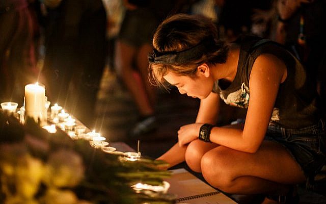 A woman in Hong Kong writes a message of support in a book placed in front of candles left by other attendees of a vigil for the victims of the Orlando shooting in Florida, June 13, 2016. (Anthony Wallace/AFP)