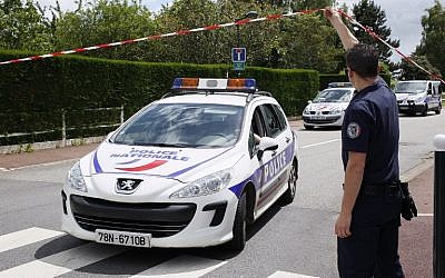 A photo taken on June 14, 2016 in Magnanville, shows a French police officer lifting the cordon as a police vehicle leaves the street where a man claiming allegiance to the Islamic State group killed a French policeman and his partner on the night of June 13.(AFP/MATTHIEU ALEXANDRE)