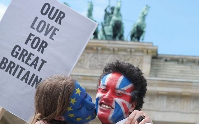 A young couple with faces paint in European, left, and British colors, pose with a sign 'Our Love For Great Britain' during a Kiss Marathon event at Brandenburg Gate in Berlin, Germany, Sunday June 19, 2016 to support the ' Remain' voters in Britain's referendum.  (Joerg Carstensen/dpa via AP)