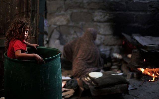 In this Monday, June 20, 2016 photo, a Palestinian girl plays in a barrel as her mother bakes bread for a Ramadan dinner at their house in el-Zohor slum, on the outskirts of Khan Younis refugee camp, southern Gaza Strip. (AP Photo/ Khalil Hamra)
