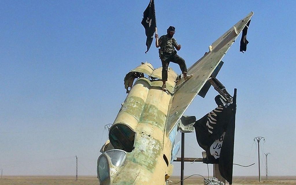 This undated file image posted by the Raqqa Media Center, in Islamic State-held territory, on Wednesday, Aug. 27, 2014, IS fighters wave the group's flag from a damaged display of a government fighter jet following the battle for the Tabqa air base, in Raqqa, Syria. (Raqqa Media Center via AP, File)