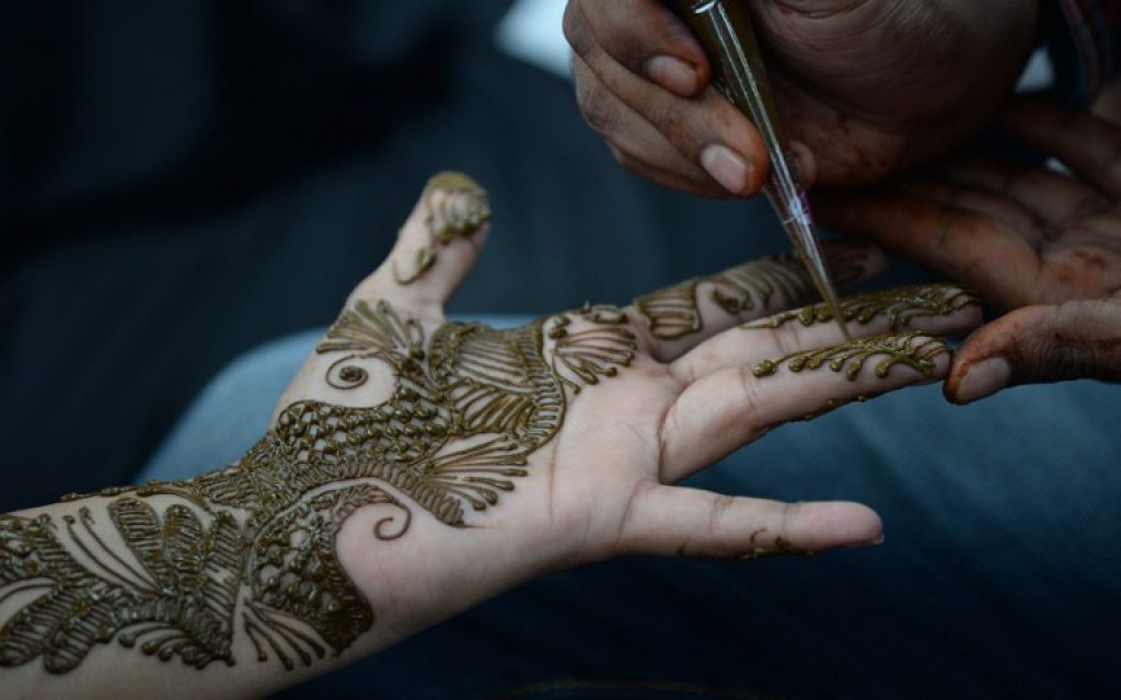 An Indian girl has decorative henna designs applied to her hands at a roadside stall ahead of the Muslim holiday of Eid al-Fitr which marks the end of Ramadan in Mumbai on July 6, 2016. (AFP PHOTO / INDRANIL MUKHERJEE)