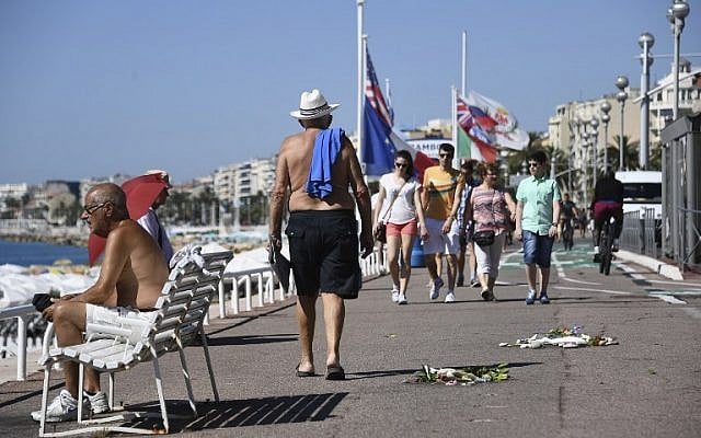 People walk on the Promenade des Anglais next to flowers left as a tribute to victims of the Bastille day deadly attack on July 17, 2016 in Nice. (AFP/ANNE-CHRISTINE POUJOULAT)