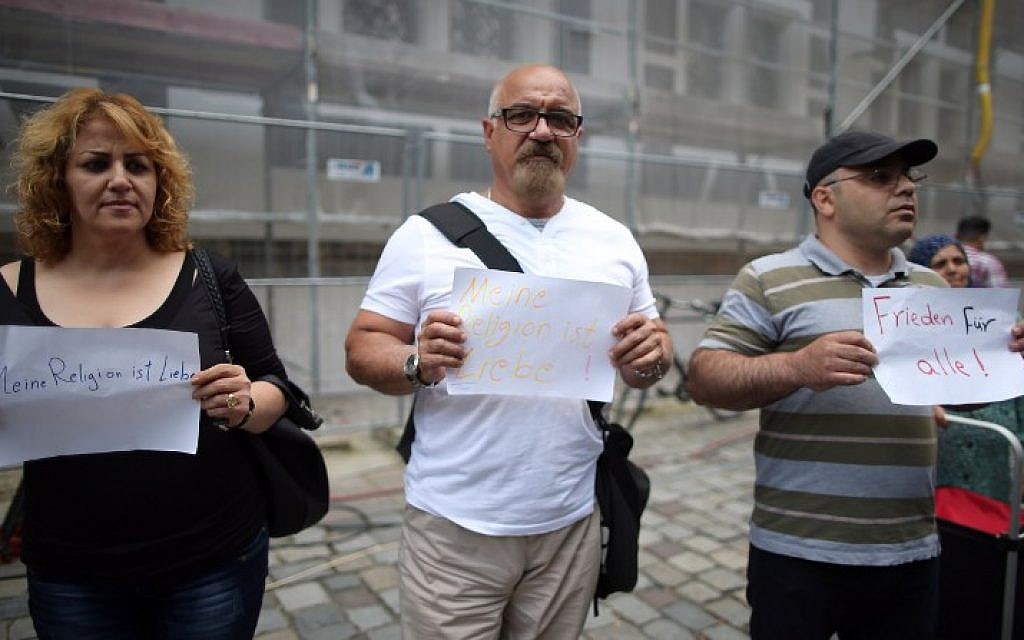 Iraqi and Syrian refugees hold signs reading 'My religion is love' and 'Peace for everybody,' near the site of a suicide bombing attack in Ansbach, southern Germany, on July 26, 2016, a day after the 27-year-old bomber wounded 15 people. (AFP PHOTO/dpa/Daniel Karmann)