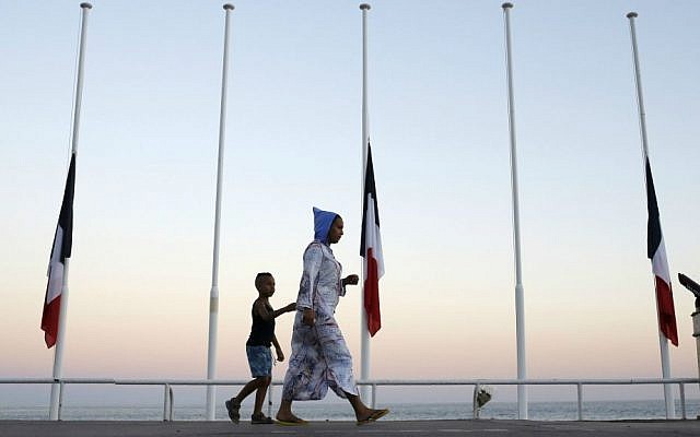 A woman and her child pass by French flags at half mast near the site of a deadly attack on the famed Boulevard des Anglais in Nice, southern France, Saturday, July 16, 2016. (AP Photo/Laurent Cipriani)