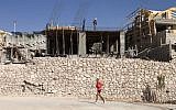 An Israeli jogs past Palestinians working at a construction site in the West Bank settlement of Ma'ale Adumim, near Jerusalem. (AP Photo/Dan Balilty)