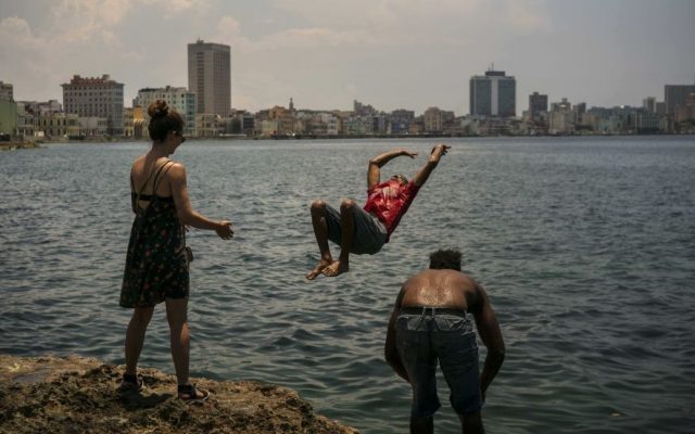 Young Cuban American Maggie Sivit, left, looks at a youth jump into the ocean from the Havana's waterfront in Cuba. Sivit was brought to the island by CubaOne, a new program inspired by the reestablishment of diplomatic and business ties between the US and Cuba. (AP Photo/Ramon Espinosa)