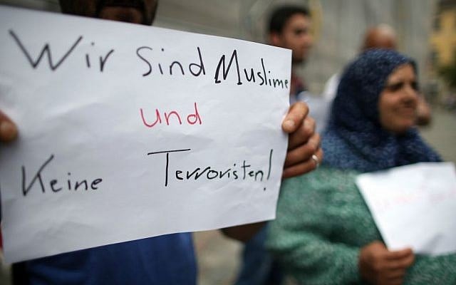 Refugees from Syria stand near the site of a terror attack in Ansbach, Germany and hold up a sign reading, 'We are Muslims and not terrorists,' Tuesday July 26, 2016. (Daniel Karmann/dpa via AP)