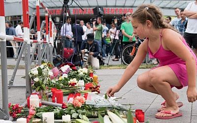 A girl puts down flowers in front of the Olympia shopping center were a shooting took place, leaving nine people dead the day before on Saturday, July 23, 2016 in Munich, Germany. (AP Photo/Sebastian Widmann)