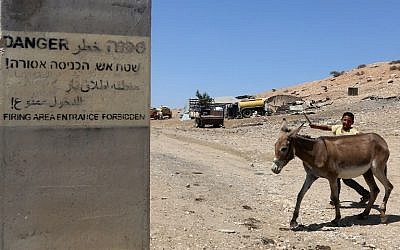 A Palestinian boy walks a donkey on a road in the West Bank area of Tubas, on July 19, 2016, near a sign on a concrete block which reads in Hebrew, Arabic and English "Firing area entrance forbidden."
(AFP PHOTO / JAAFAR ASHTIYEH)