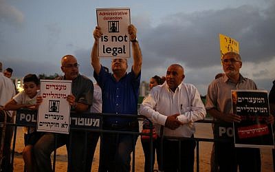Illustrative: Arab MK Ahmad Tibi (C) holds a poster against administrative detention during a demonstration in support of Palestinian prisoner Bilal Kayed (portrait), who has been fasting for 53 days over his detention without trial, as they demonstrate outside the Ashkelon hospital where he is being held on August 9, 2016. (AFP Photo/Ahmad Gharabli)