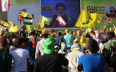 Young men hold Lebanese national flags and yellow flags of the Lebanese Shiite terror group Hezbollah as they watch its leader Hassan Nasrallah deliver a speech on a screen in the southern Lebanese town of Bint Jbeil on August 13, 2016 during a commemoration marking the tenth anniversary of the end of the Second Lebanon War. (AFP Photo/Mahmoud Zayyat)