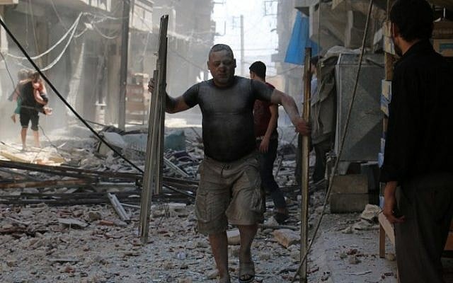 A Syrian man covered with dust carries pieces of metal on a street cluttered with rubble following a reported air strike on the rebel-held neighbourhood of Sakhur in the northern city of Aleppo, on August 15, 2016. (AFP PHOTO / AMEER ALHALBI)