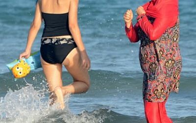 Illustrative: Women, one, wearing a 'burkini,' a full-body swimsuit designed for Muslim women, walk in the water on Ghar El Melh beach near Bizerte, north-east of the capital Tunis, August 16, 2016.  (AFP/FETHI BELAID)