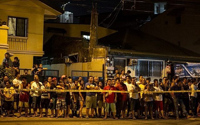 This photo taken on July 19, 2016 shows residents behind a police line looking at the two dead bodies of an alleged drug dealer after a drug bust operation that turned into a gun fight in Manila. (AFP PHOTO / NOEL CELIS)