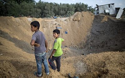 Illustrative. Palestinian children stand next to a crater in Beit Lahiya in the northern Gaza Strip on August 22, 2016, following an Israeli airstrike the night before that targeted Hamas positions in response to a rocket fired from the Palestinian enclave that hit the Israeli city of Sderot. (Mahmud Hams/AFP)