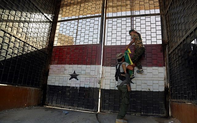 Kurdish fighters belonging to the People's Protection Units (YPG) put a YPG flag on the door of the central prison in the northeastern Syrian city of Hasakeh on August 23, 2016, after they agreed to a truce with regime forces. (AFP PHOTO/DELIL SOULEIMAN)