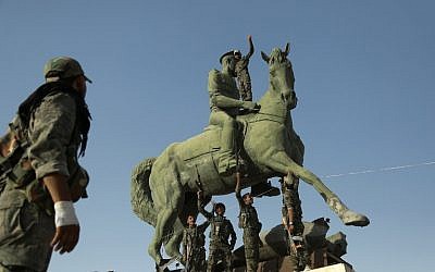 Kurdish fighters belonging to the police force -- the Asayesh -- and the People's Protection Units (YPG) stand on a statue of Basel Assad, the late elder brother of the Syrian President, in the northeastern Syrian city of Hasakeh on August 23, 2016, after they agreed to a truce with regime forces. (AFP PHOTO/DELIL SOULEIMAN)