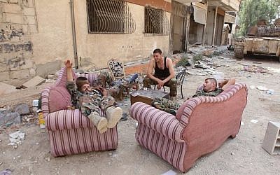 Syrian army soldiers sit on furniture placed in the street in the government-controlled part of the besieged town of Daraya on August 26, 2016, as thousands of rebel fighters and civilians prepared to evacuate. (AFP PHOTO/Youssef KARWASHAN)