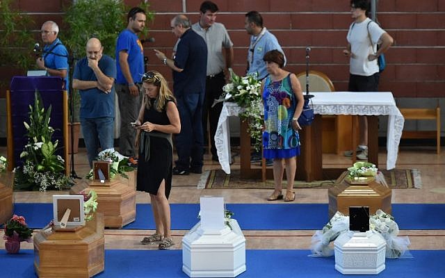 People stand next to the coffins of earthquake victims, in a gymnasium arranged in a chapel of rest on August 26, 2016, in Ascoli Piceno, two days after a 6.2-magnitude earthquake struck the region killing 281 people. (AFP PHOTO/ALBERTO PIZZOLI)