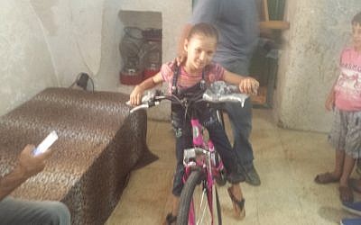 Anwar Burqan, an 8-year-old Palestinian whose bicycle was destroyed by two border guards in Hebron, tries out a new bicycle purchased for her by an Israeli man on August 17, 2016. (Lonny Baskin)
