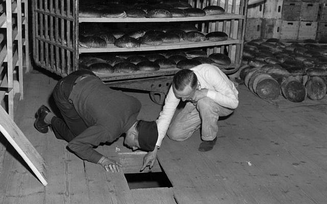 In this April 1946 photo US Lt. Robert R, Rogers, left, and Erich Pinkau, of the German criminal police, examine the under-floor hiding place where arsenic was found in a Nuremberg, Germany bakery which supplied bread to Stalag 13. (US Army Signal Corps via AP)