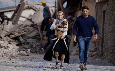 A woman holds a dog in her arms as she walks with a man next to the rubble of buildings in Amatrice on August 24, 2016 after a powerful earthquake rocked central Italy. AFP PHOTO / FILIPPO MONTEFORTE