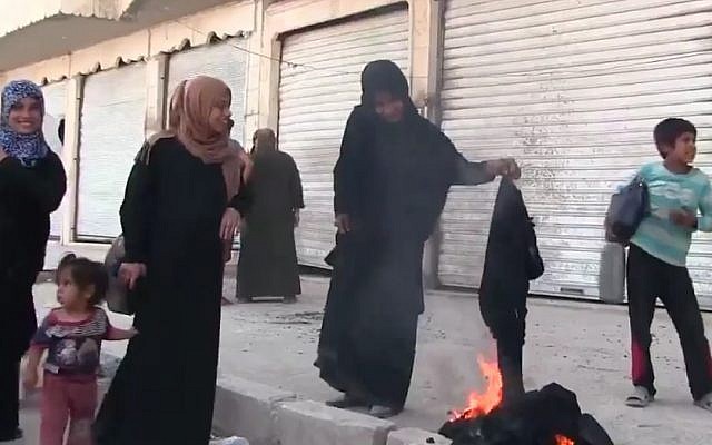 A Syrian woman burning a burqa in celebration of the freeing of the town of Manbij from IS control, August 13, 2016. (Screenshot/K24)