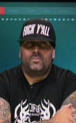 Far-right rapper Yoav Eliasi, a.k.a. The Shadow, is interviewed on Channel 2 on October 12, 2015. His hat says, 'Fuck y'all.' (screen capture)