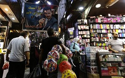 A poster of the Syrian President Bashar al-Assad and reading in Arabic: " Assad is with you forever" hangs above Syrians shopping at the Hamidiyeh popular market in the old part of the capital Damascus as they prepare for the Muslim Eid al-Adha holiday on September 11, 2016. (AFP PHOTO / LOUAI BESHARA)/