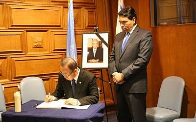 UN Secretary General Ban Ki-Moon, seated, signs a commemoration book for former Israeli president Shimon Peres at a memorial ceremony held at UN Headquarters in New York, September 29, 2016. Standing is Israel's envoy to the world body Danny Danon. (Courtesy)