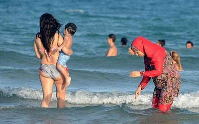 A Tunisian Muslim woman, right, wearing a burkini swimsuit wading in the water on a beach near Tunis, August 16, 2016. (Fethi Belaid/ AFP/Getty Images/JTA)