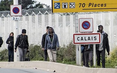 Migrants and refugees walk next to a roadside reading 'Calais' near the 'Jungle' migrant camp on October 19, 2016 (AFP/Denis Charlet)