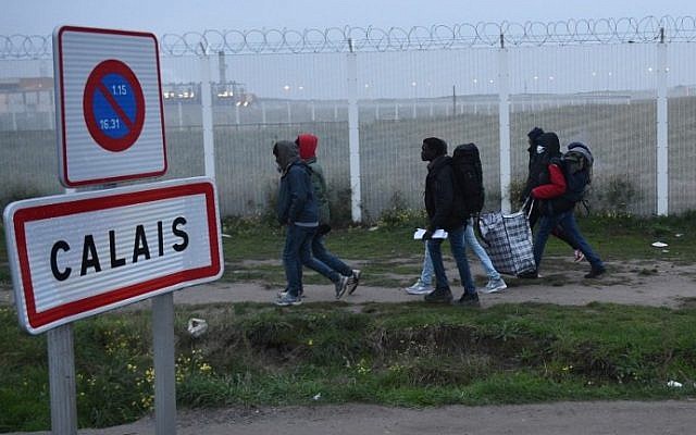 Migrants, carrying their luggage, walk past a Calais city limit sign as they evacuate the "Jungle" camp, in northern France, on October 24, 2016. (AFP PHOTO / FRANCOIS LO PRESTI)