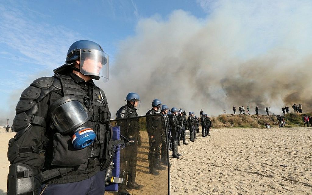 French gendarmes stand together as smoke rises from fires at the "Jungle" migrant camp in Calais, northern France, on October 26, 2016, during a massive operation to clear the settlement. (AFP PHOTO / François NASCIMBENI)