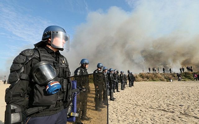 French gendarmes stand together as smoke rises from fires at the "Jungle" migrant camp in Calais, northern France, on October 26, 2016, during a massive operation to clear the settlement. (AFP PHOTO / François NASCIMBENI)