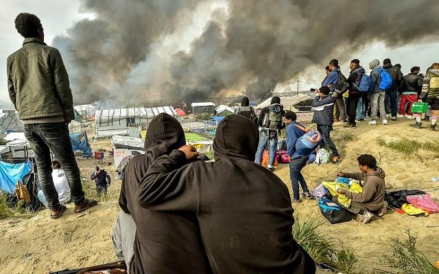 Migrants looks at the smoke rising from fires in the "Jungle" migrant camp in Calais, northern France, on October 26, 2016, during a massive operation to clear the squalid settlement where 6,000-8,000 people have been living in dire conditions. (Philippe Huguen/AFP) Migrants looks at the smoke rising from fires in the "Jungle" migrant camp in Calais, northern France, on October 26, 2016, during a massive operation to clear the squalid settlement where 6,000-8,000 people have been living in dire conditions. (Philippe Huguen/AFP)