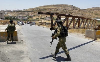 An Israeli soldier closes a gate at a checkpoint in the West Bank village of Yatta, near Hebron, on July 3, 2016. (Wisam Hashlamoun/Flash90)