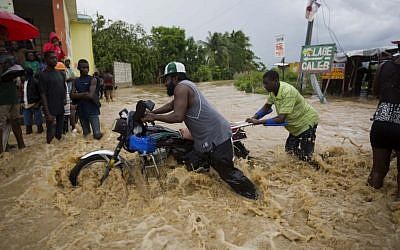Men push a motorbike through a street flooded by a river that overflowed from heavy rains caused by Hurricane Matthew in Leogane, Haiti, Wednesday, October 5, 2016. (AP Photo/Dieu Nalio Chery)