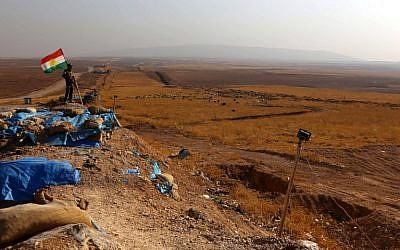 An Iraqi Kurdish Peshmerga fighter, next to a Kurdish flag, holds a position in Sheikh Ali village near the town of Bashiqa, some 25 kilometers north east of Mosul, on November 6, 2016, during an operation against IS jihadists to retake the main hub city. (AFP Photo/Safin Hamed)