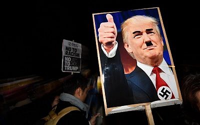 A demonstrator holds a placard showing a picture of US President-elect Donald Trump modified to add a swastika and an Adolf Hitler-style moustache during a protest outside the US Embassy in London November 9, 2016 against Trump after he was declared the winner of the US presidential election. (AFP PHOTO / BEN STANSALL)
