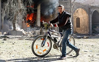 A Syrian youth pushes his bicycle past a burning house on November 19, 2016 following a reported air strike on Aleppo's rebel-held neighborhood of Bab al-Nayrab. (Ameer Alhalbi/AFP)