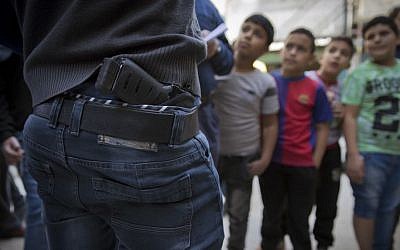 In this photo taken Thursday, Novemver 10, 2016, Palestinian refugee boys gather by armed men who are wanted by the Palestinian Authority security, one with a concealed weapon, in Balata refugee camp, in the West Bank. (AP Photo/Nasser Nasser)