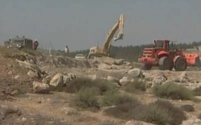A bulldozer levels land for a construction project in the West Bank, as Israeli soldiers look on. (YouTube screenshot)